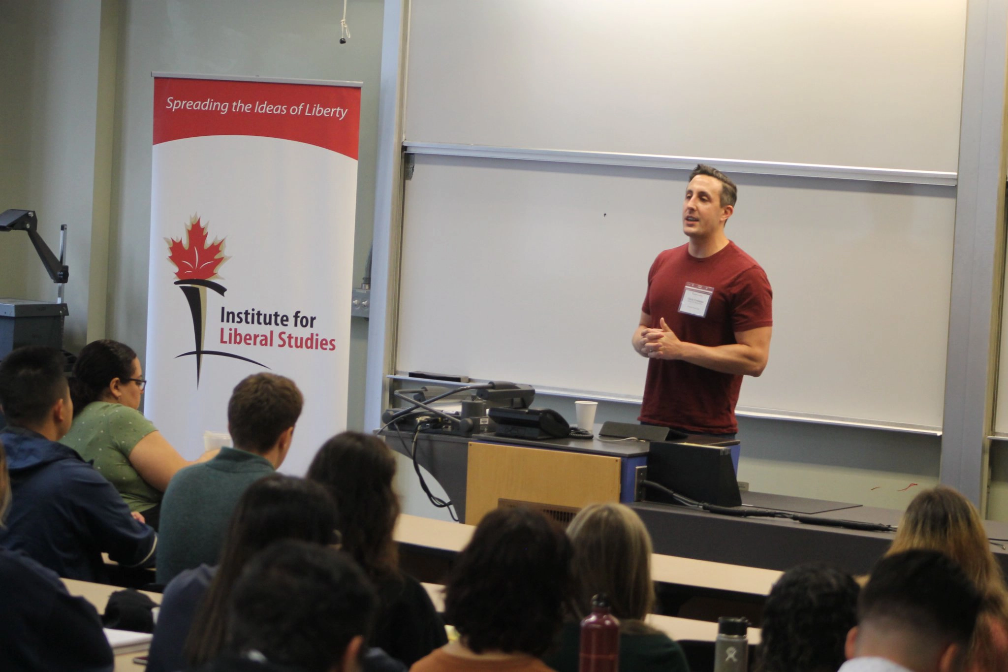 A speaker address a classroom with a ILS banner at the side of the room