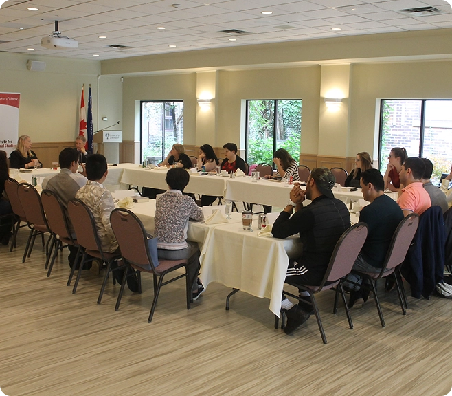 A group of people sit around several tables listening to a discussion